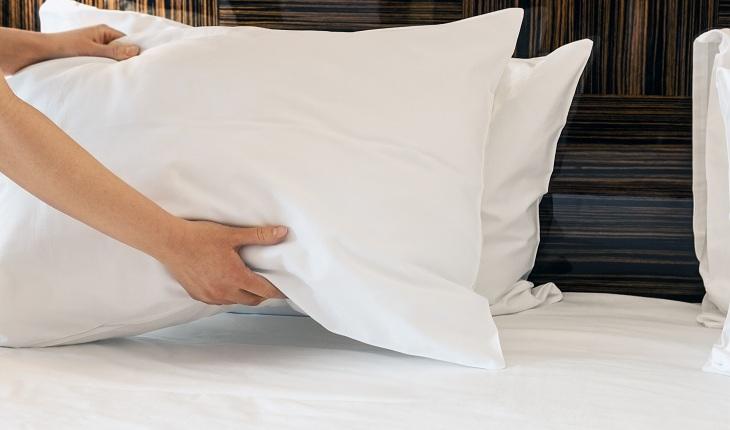 A foto mostra uma pessoa arrumando travesseiro na cama.