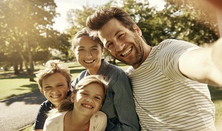 Família de 4 membros sorrindo ao ar livre para tirar uma foto
