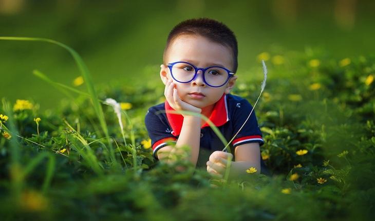 nomes italianos: imagem de um garoto sentado em um gramado vestindo uma camiseta polo e um óculos azul.