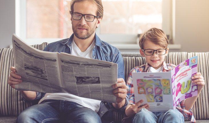 Pai lendo jornal com o filho no sofá para manter a família sempre protegida