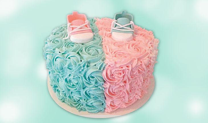 bolo revelação decorado metade com glacê azul e a outra aprte com glacê cor-d-rosa, sapatinhos de bebe em cima
