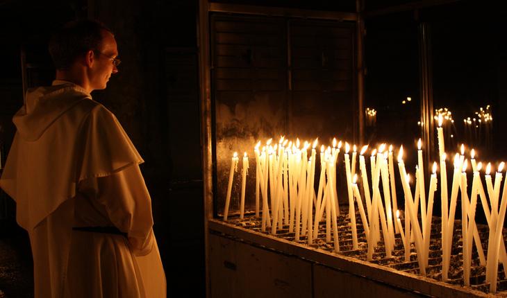 Imagem d eum padre olhando para uma série de velas de grande porto em um altar. Provérbios da semana