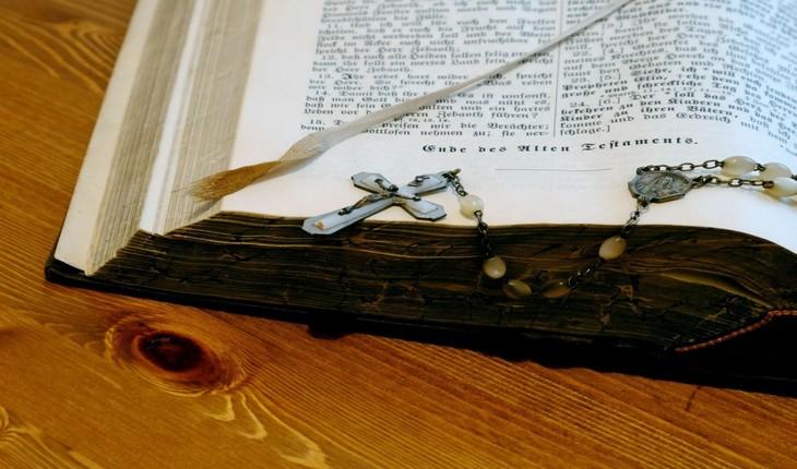 Imagem de uma bíblia aberta em uma superfície de madeira com um crucifixo marcando algumas de suas páginas. Provérbios da semana