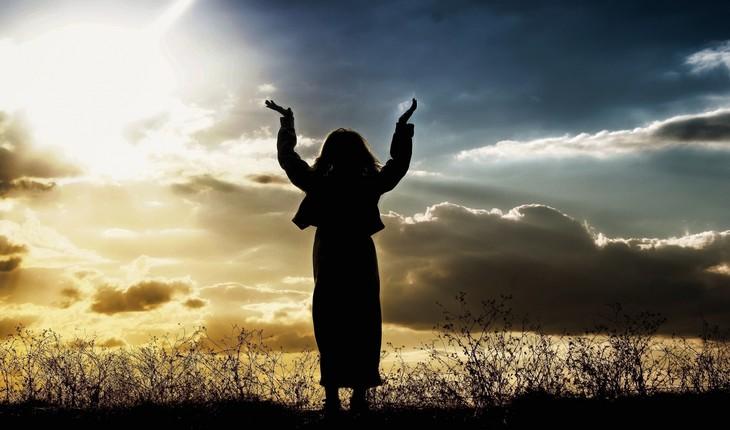 Imagem de uma mulher em uma colina com as mãos para cima durante o por do sol. Provérbios da semana