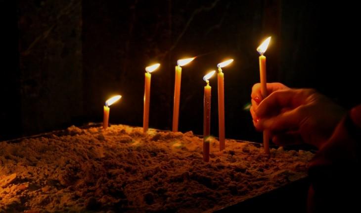 Imagem de algumas velas acesas em um quarto escuro sendo, algumas delas, seguradas por uma mão. Provérbios da semana