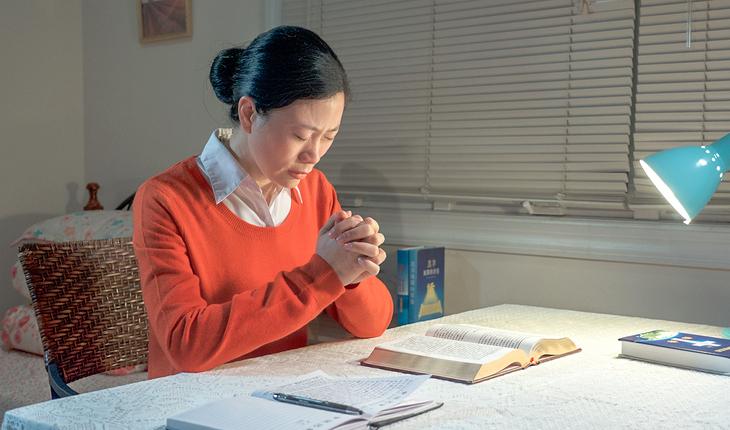 Imagem de uma mulher de origem asiática sentada em uma mesa orando. Sobre a mesa há alguns livros abertos. Provérbios da semana