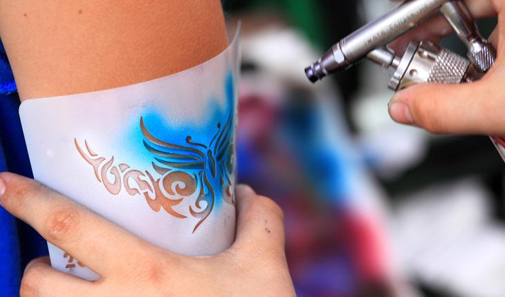 pessoa segurando um molde e fazendo uma air brush tattoo no braço de outra