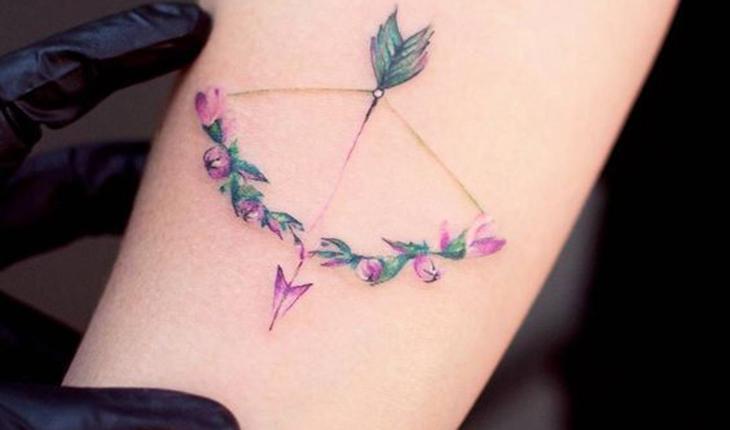tatuagem de de um aco e flecha nas cores verde, rosa e roxo