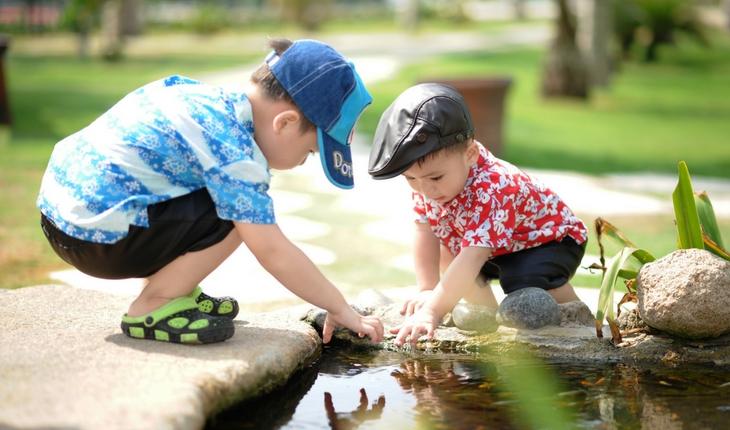 Dois bebês brincam com água, estão usando chapéus