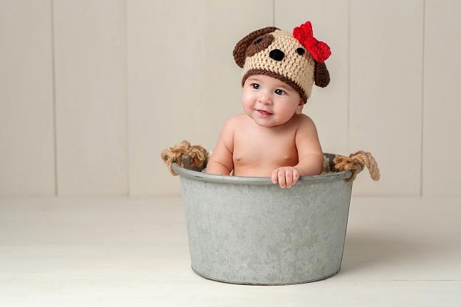 imagem de um bebê com uma toca de crochê em formato de cachorro sentado dentro de um balde