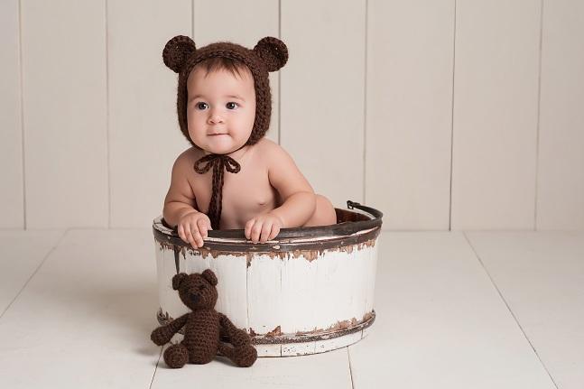 imagem de um bebê com uma toca de crochê em formato de orelha de urso sentado dentro de uma tina