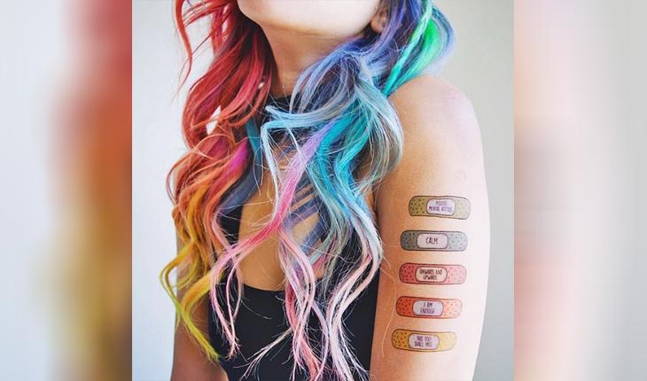 foto mostrando do maxilar para baixo de uma mulher com cabelo colorido e tatuagens de decalque contra a ansiedade e depressão no braço