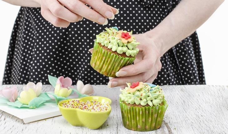mãos femininas decorando cupcakes com confeitos