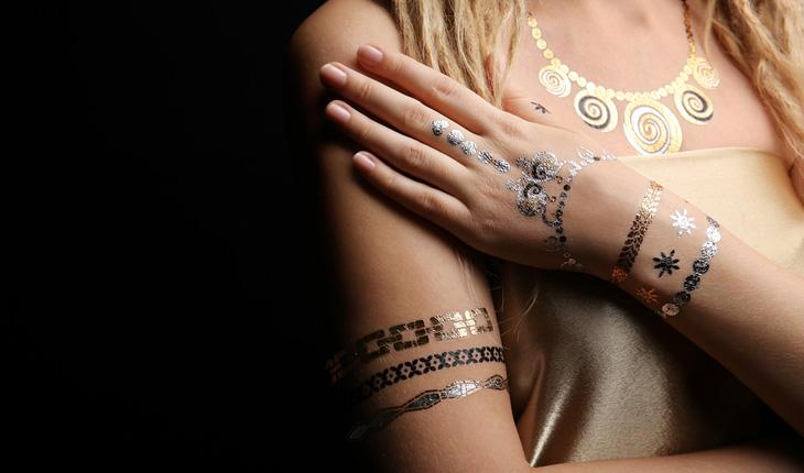 mulher com flash tattoos ao redor do braço e na mão nas cores prata e dourada