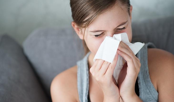 Foto com mulher gripada assoando o nariz