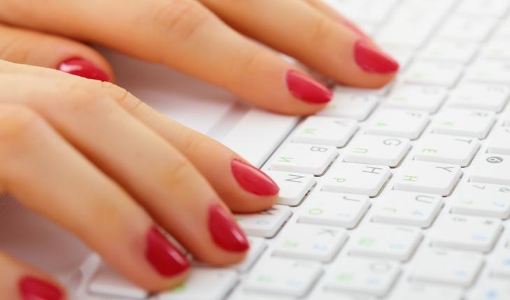 mulher de esmalte vermelho digitando em teclado branco