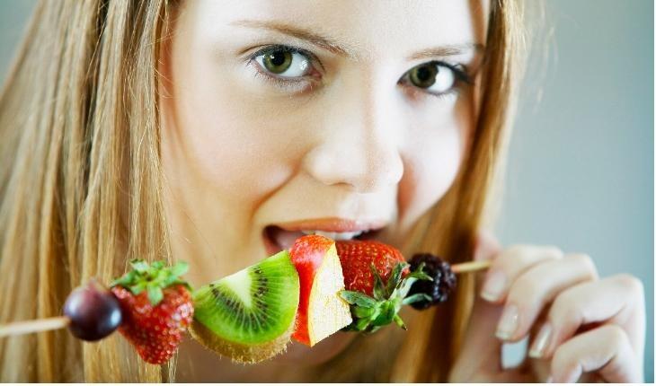 Menina loira comendo espetinho de frutas variadas