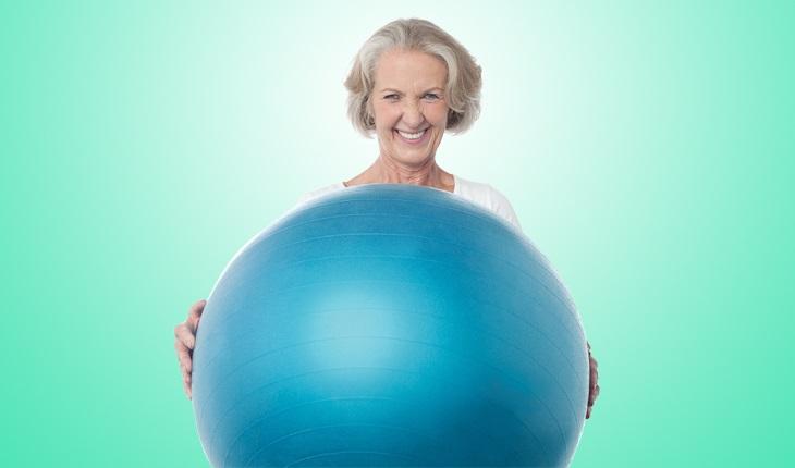 Mulher idosa segurando uma bola de pilates e sorrindo. Exercícios recomendados na terceir