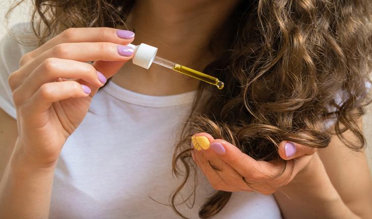 mulher loira pingando um produto nas pontas do cabelo com um conta gotas