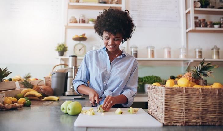 mulher sorrindo e picando frutas na cozinha