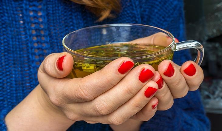 mãos de uma mulher segurando xícara de chá verde