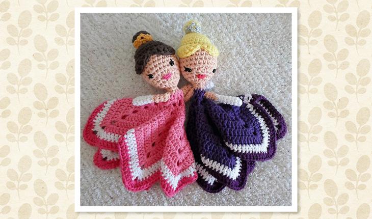 Na foto há 2 naninhas de crochê de princesas. Uma princesa é loira com vestido (manta) rosa e a outra é morena e tem a roupa rosa.