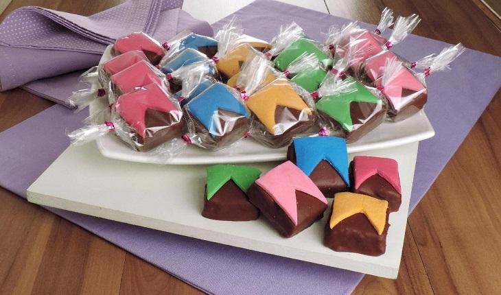 paçocas cobertas de chocolate e decoradas com bandeirinhas coloridas sobre um travessa branca