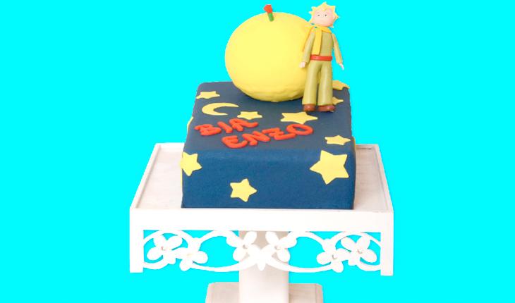 bolo do Pequeno Príncipe retangular azul com um planeta amarelo em cima e boneco do Pequeno Príncipe