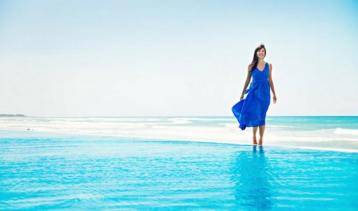 mulher de vestido azul escuro caminhando na praia de água azul clara