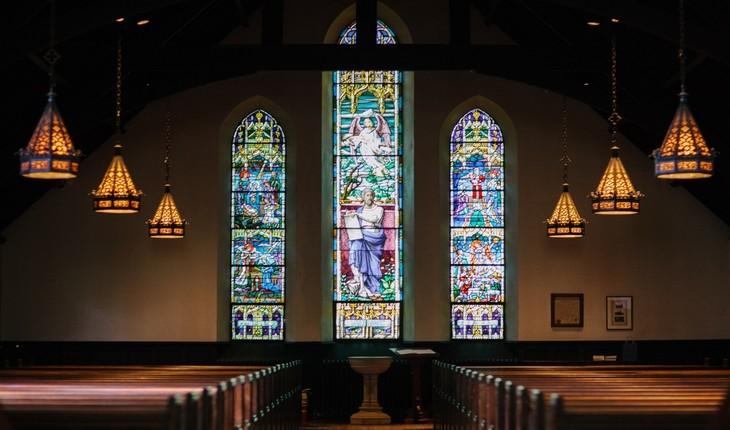 Imagem do interior de uma igreja com destaque para seus vitrais de fundo. Família sempre protegida.