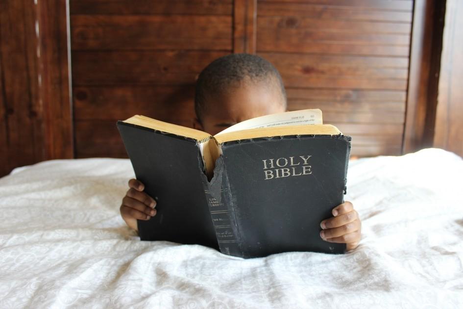 Imagem deuma criança deitada em cama, com o rosto coberto lendo uma bíblia. provérbios semanais