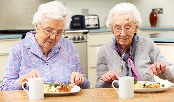 A foto mostra duas senhoras comendo alimentos indicados para envelhecer com saúde