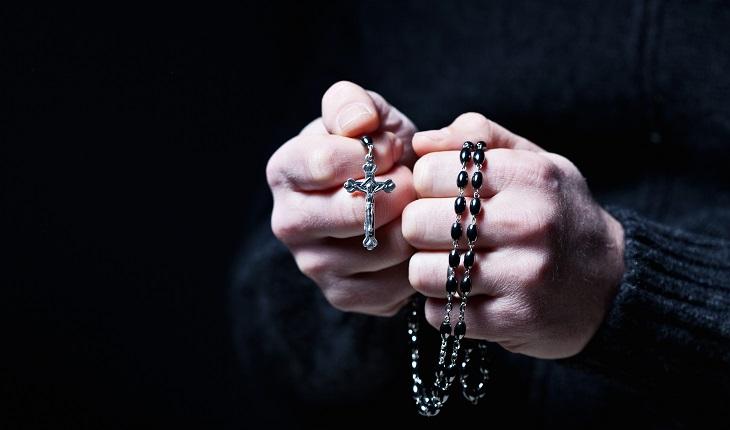 Mãos masculinas segurando um terço pensando em frases de fé