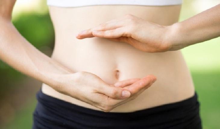 Na imagem, uma mulher com a barriga de fora está com as mãos indicando uma parte específica da barriga, o útero. Contraceptivos.