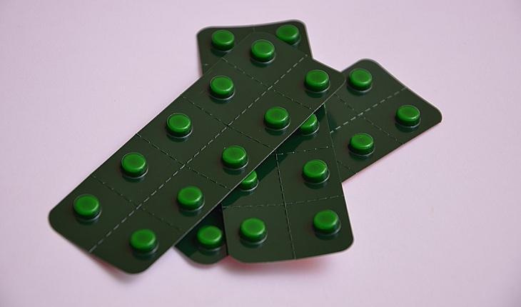 Na imagem, três cartelas de pílulas verdes está numa superfície rosa, um em cima do outro. Contraceptivos.
