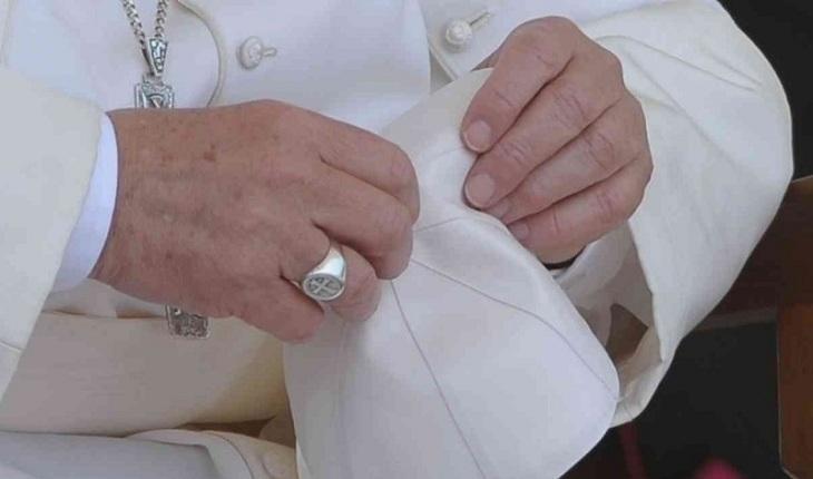 Na imagem, a mão do papa francisco segura seu chapéu simples com um anel de papado de prata e sua cruz de aço, mostrando humildade. Dia do papa.
