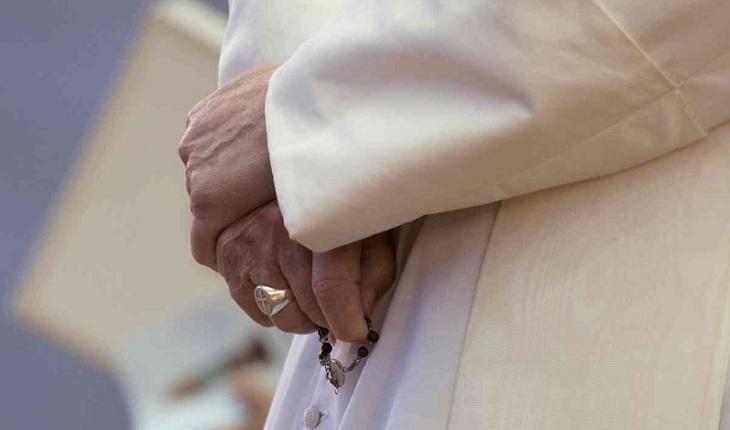 Na imagem, as mãos do papa francisco segura discretamente seu terço vermelho e reza pedindo perdão.