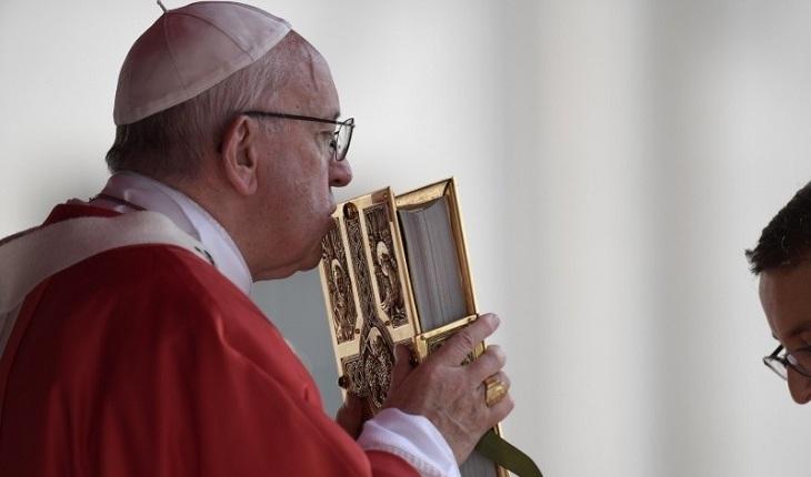 Na imagem, o papa francisco beija uma bíblia dourada em uma missa. Dia do papa.