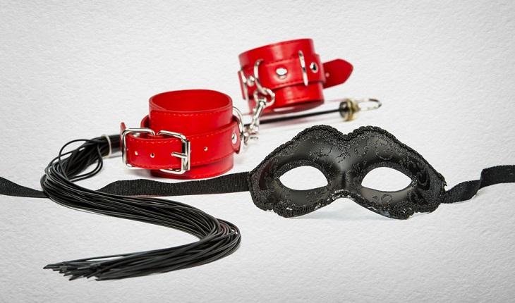 brinquedos eróticos sobre um fundo cinza, máscara preta e braceletes de couro vermelho