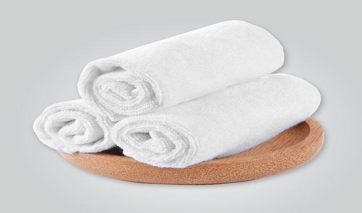 três toalhas brancas enroladas sobre uma madeira redonda