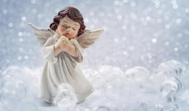 miniatura de um anjinho rezando, fundo azul claro, neve caindo