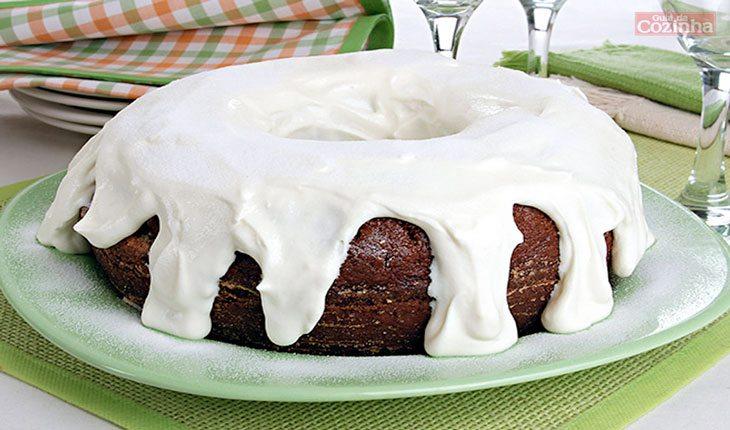 Na foto há um bolo de chocolate com cobertura de leite Ninho branca.