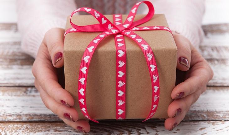 caixa de presente embalada com papel parde e com laço de fita vermelha de corações brancos