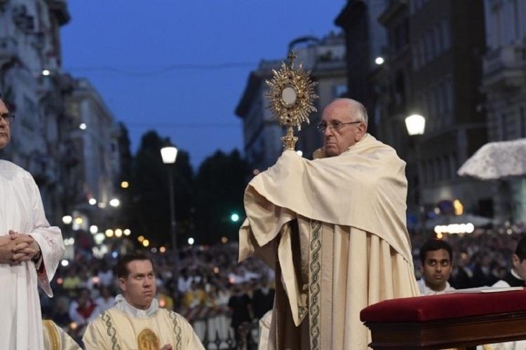 Na imagem, o Papa Francisco carrega o símbolo da Eucaristia nas mãos com olhar sério e o povo olha para o papa. Recordação de Jesus. 