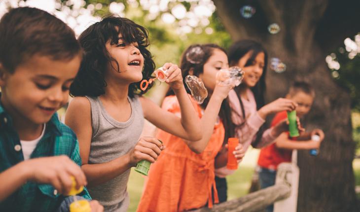 uma imagem de 5 crianças brincando com bolha de sabão