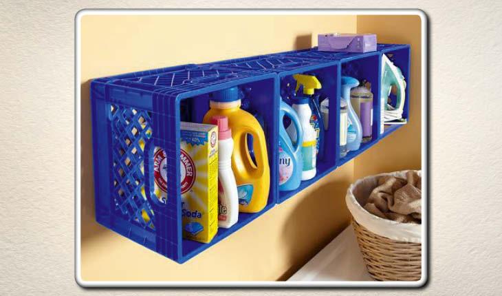 Na imagem é possível ver caixas de plástico de estilo de feira sendo utilizadas como estante dentro da lavanderia. Elas são azuis e estão com produtos.