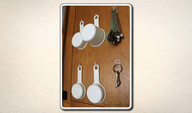 Na imagem há pequenos ganchos presos a uma porta de armário e neles há itens de cozinha pendurados, como medidores.
