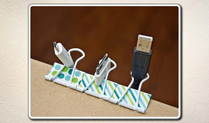 Na imagem os cabos de escritórios, como USB e de carregamento estão presos por grampos de escritório que estão no canto da mesa, deixando-os organizados.