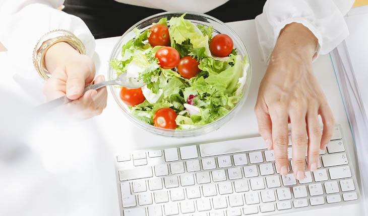 Mulher comendo salada e mexendo no computador, anti-barriga