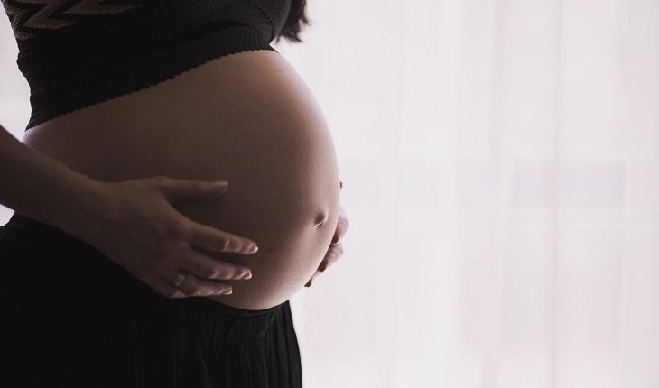 Na imagem, uma mulher grávida está com roupas pretas e barriga a mostra. Consulta ginecológica.